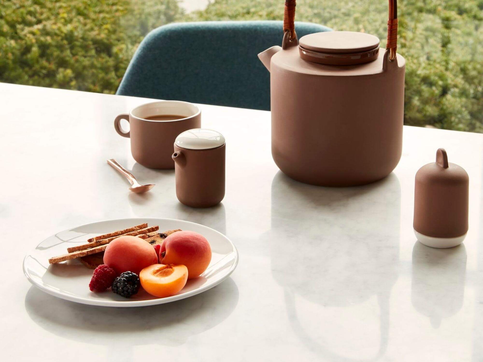 White side plate with fruit on it beside tea pot and mug