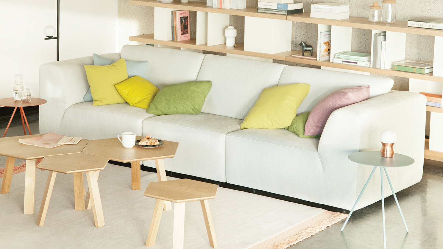 The Morten modern sectional in white fabric, covered in colorful throw pillow, in a brightly lit living room with a blue end table