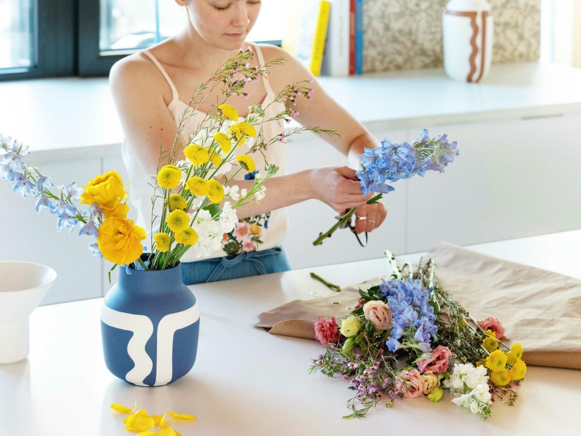 Woman preps flowers for a bouquet in a blue and white vase