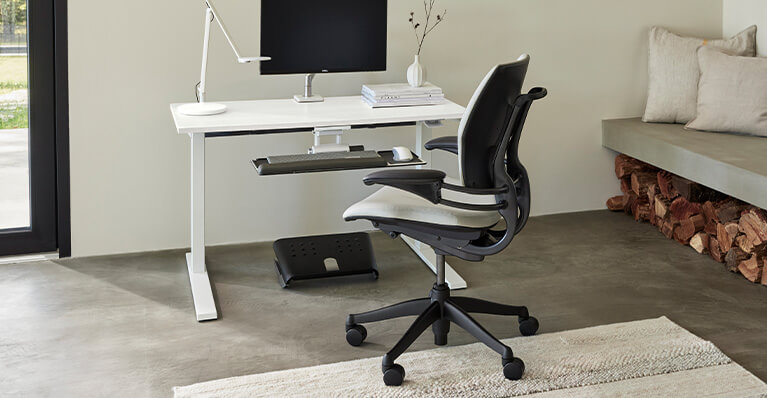 White humanscale stand up desk and office chair is shown in a home office setting. Link to humanscale category page