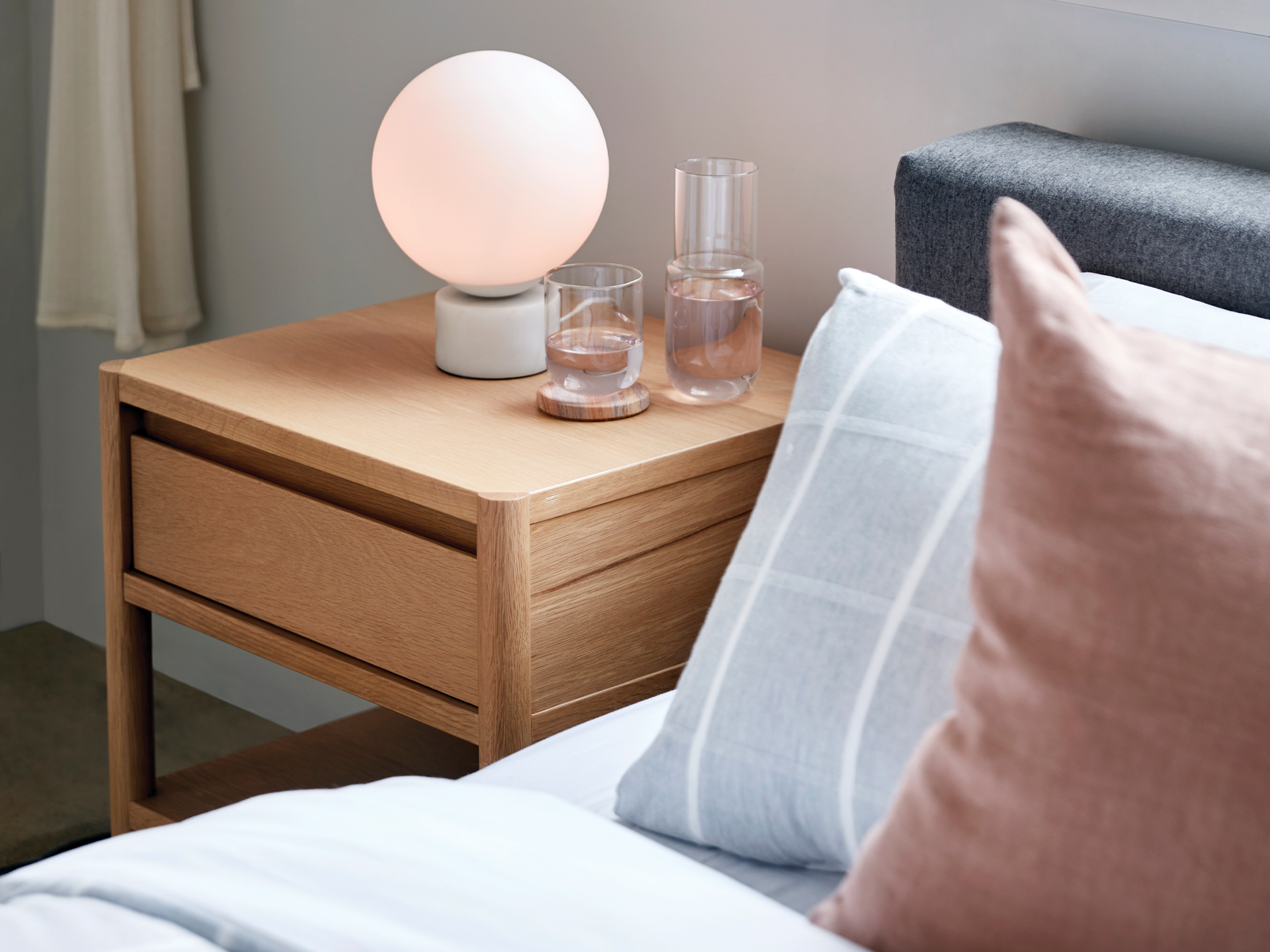 Bedside lamp with marble base and white glass shade on an oak nightstand