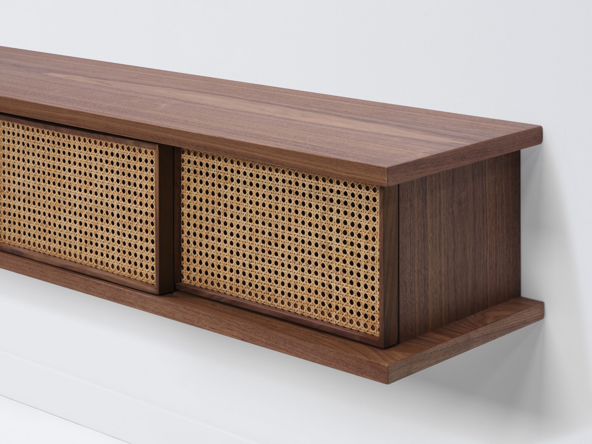 Detail view of medium walnut floating shelf with natural cane doors