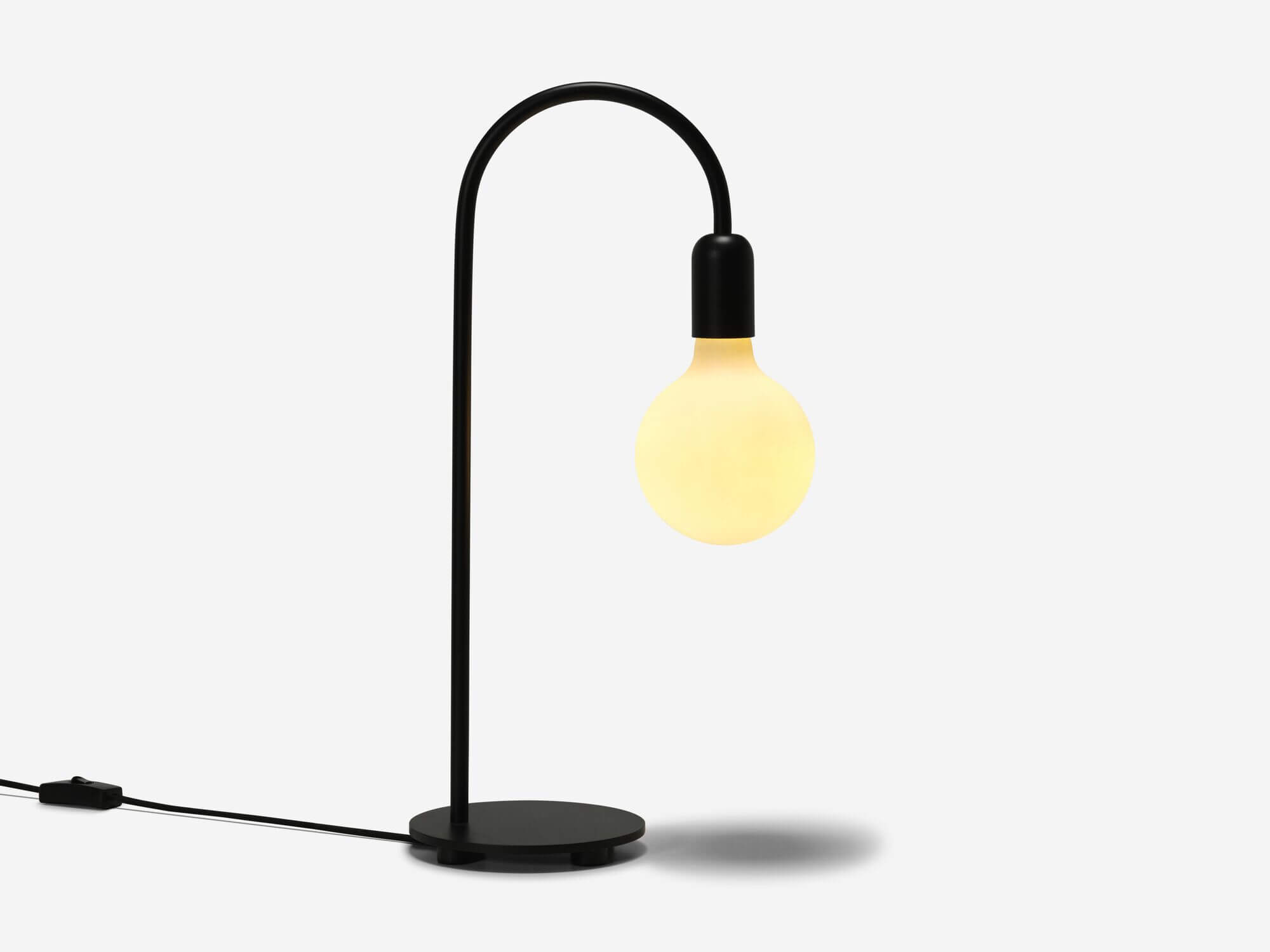 Black curved table lamp with light on side view