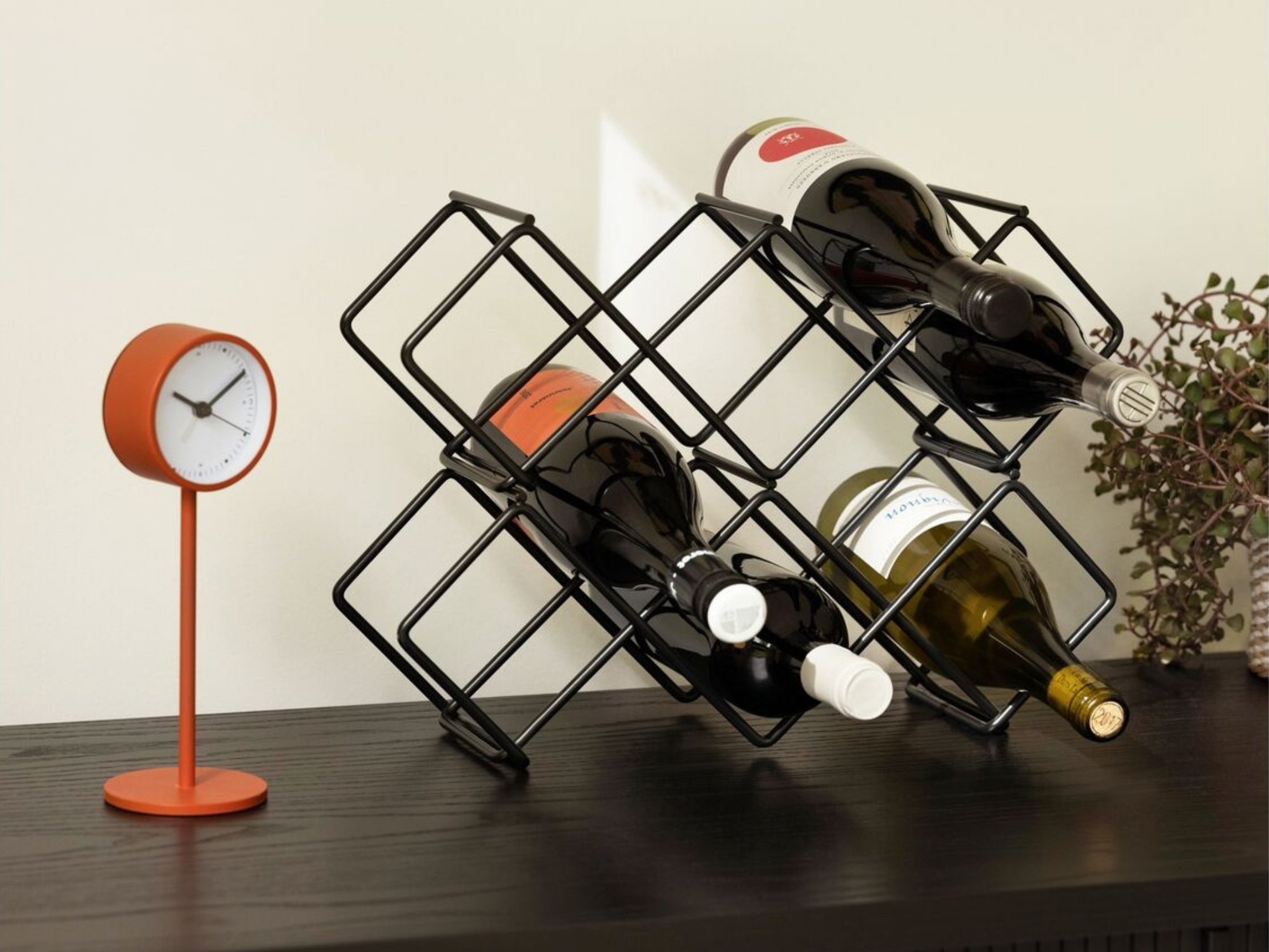 Black metal wine rack with bottles and clock on black console table