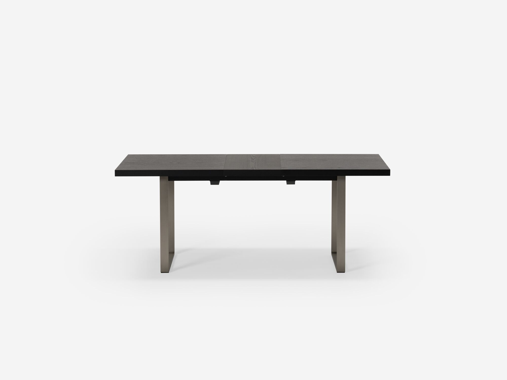 Side view of expandable dining table with stainless steel legs and black top with one leaf