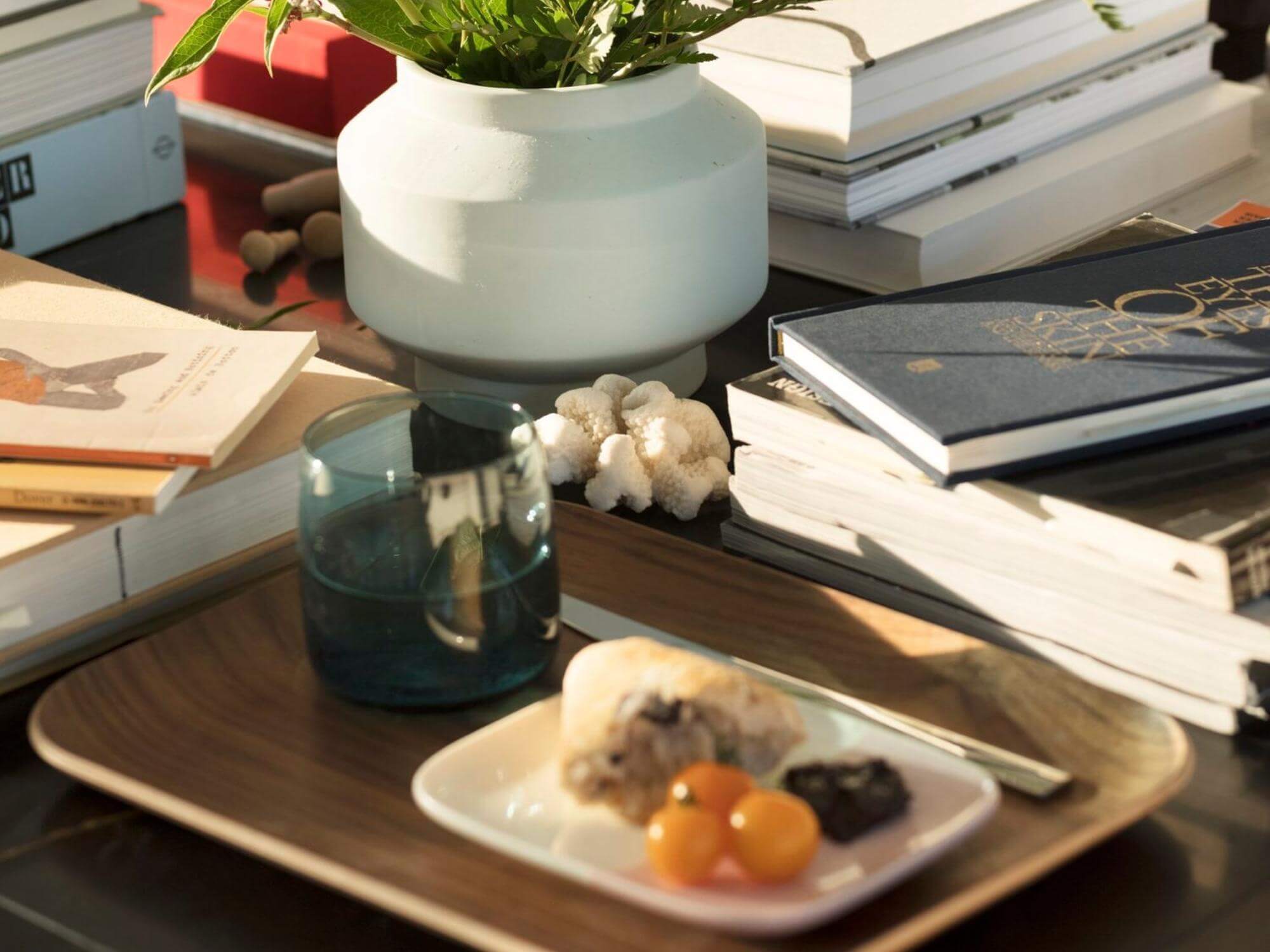 Grey glass tumbler on wood serving tray with vase and books around it