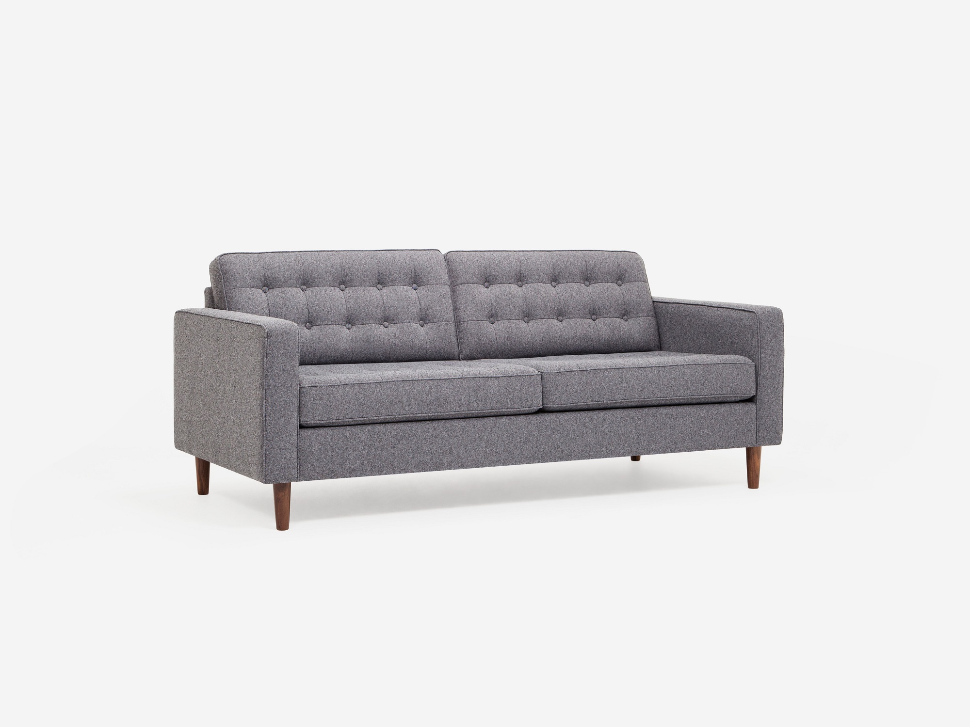 Corner view of grey tufted apartment sofa with walnut legs