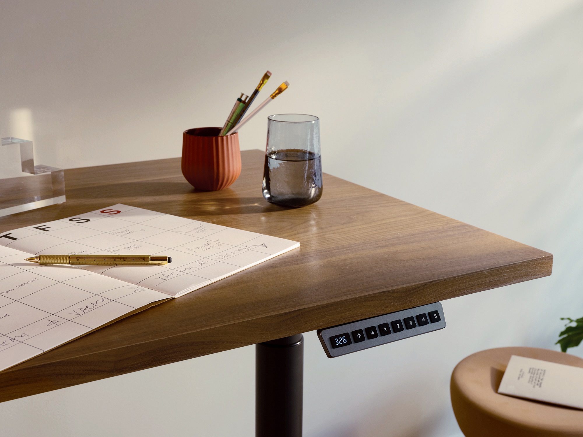 Edge of walnut standing desk with water glass and paper planner on top