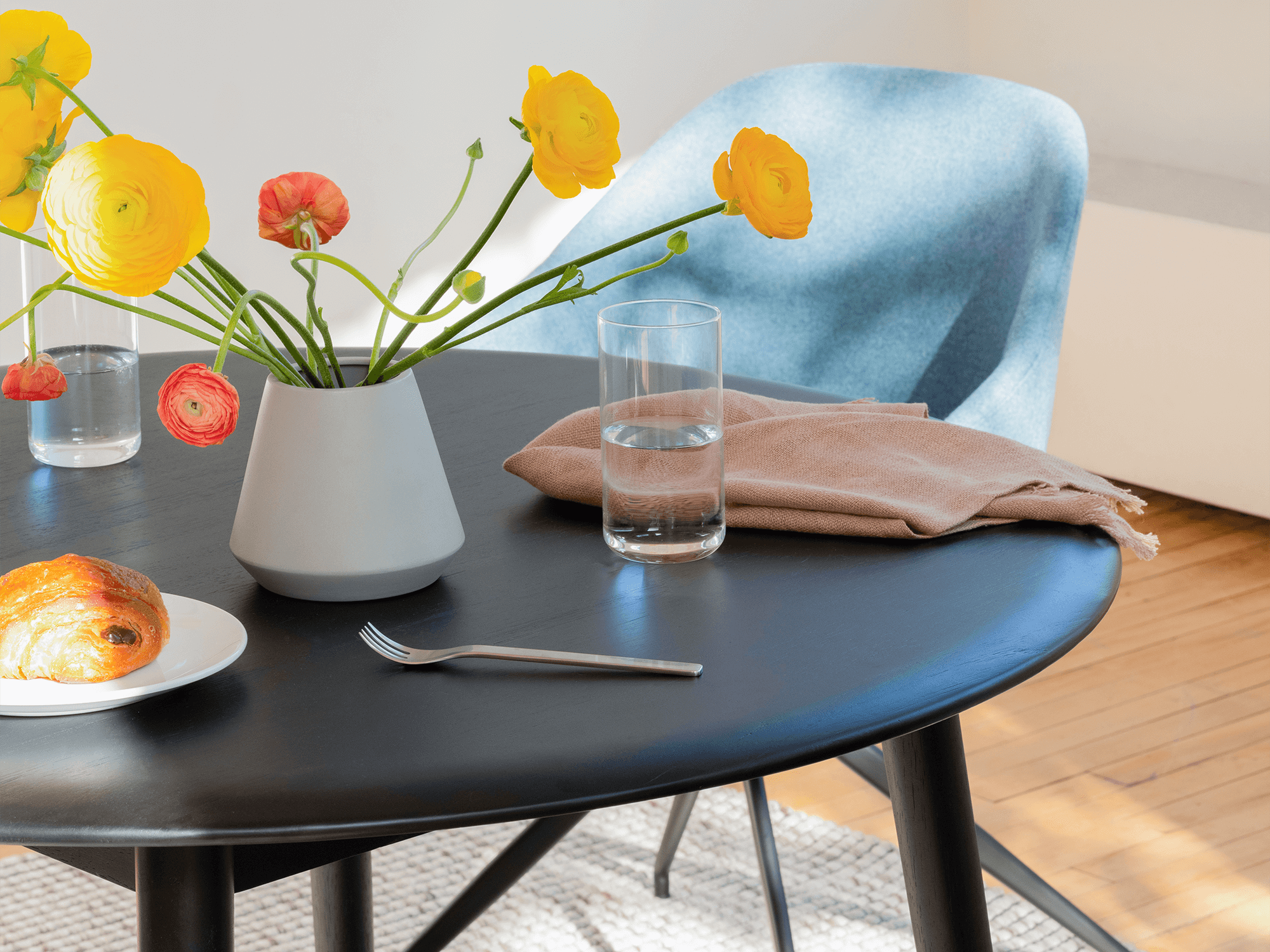 A pastry and glass of water sit on a black round dinette table with a blue chair near it