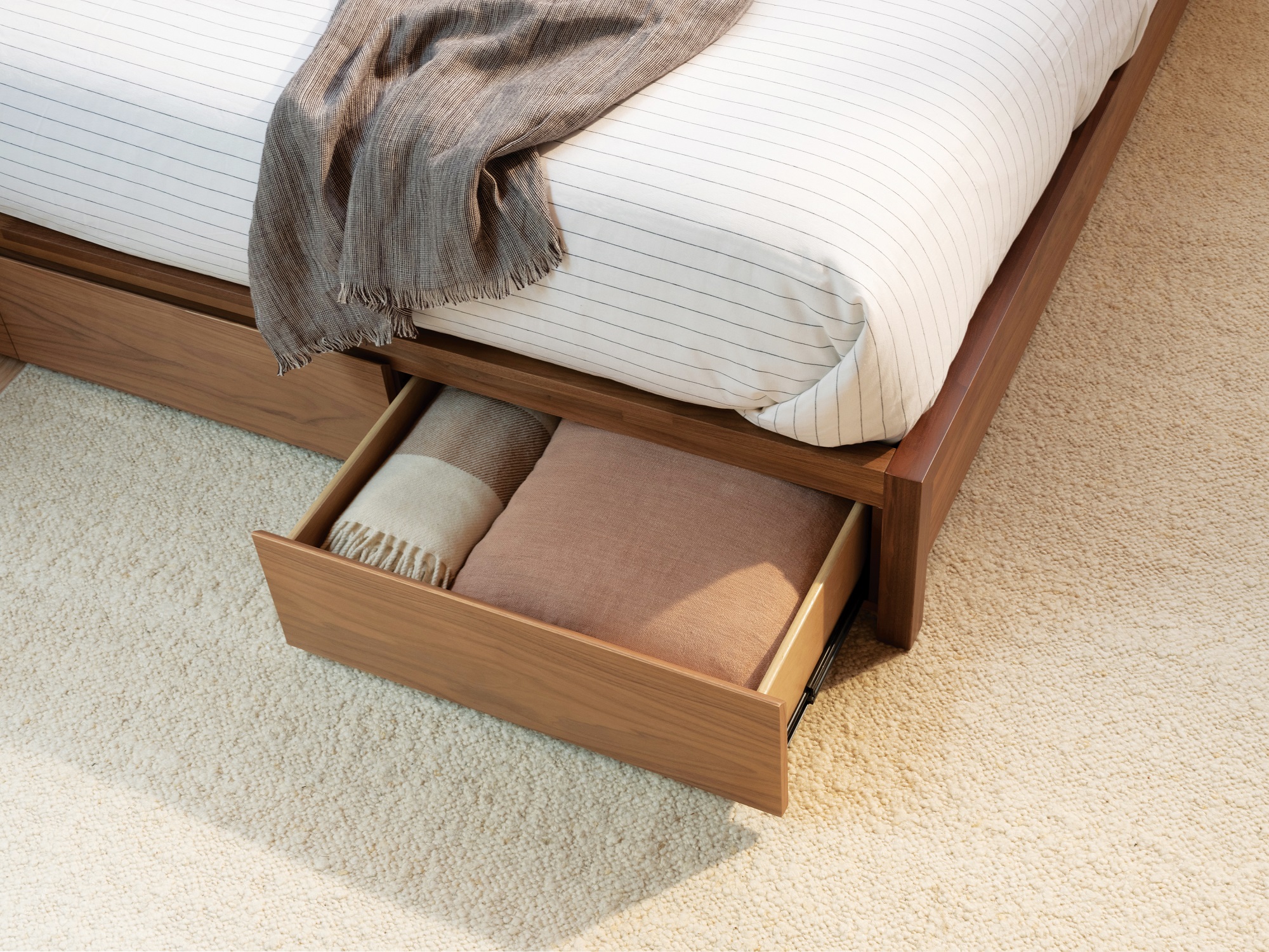 Open drawer under walnut storage bed filled with throw blankets