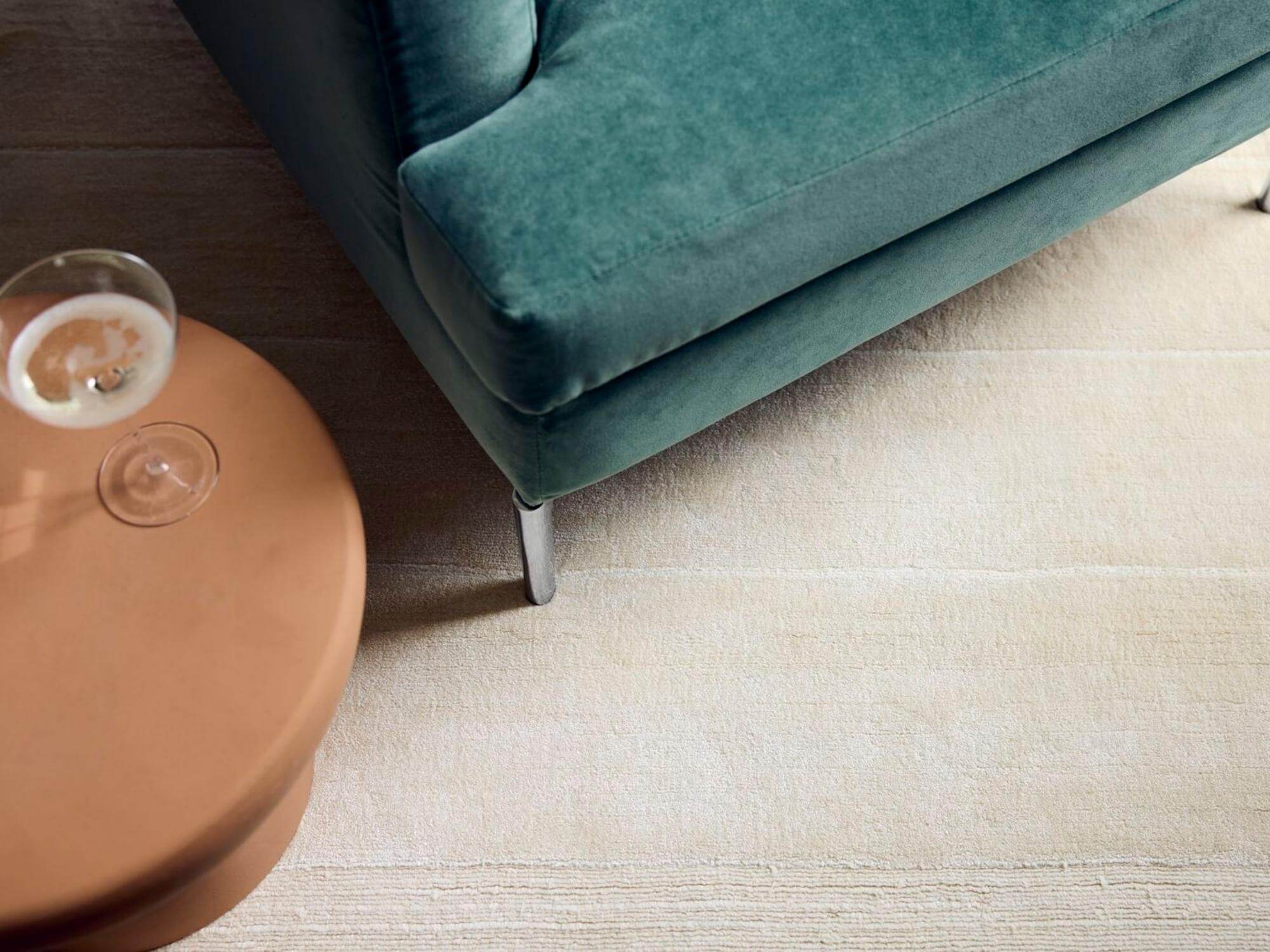 Terracotta stool with wine glass on it beside green sofa