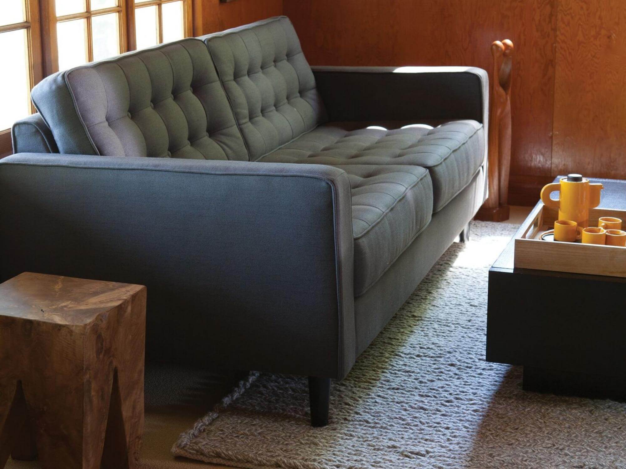 Grey tufted apartment sofa with teak stool in rustic living room