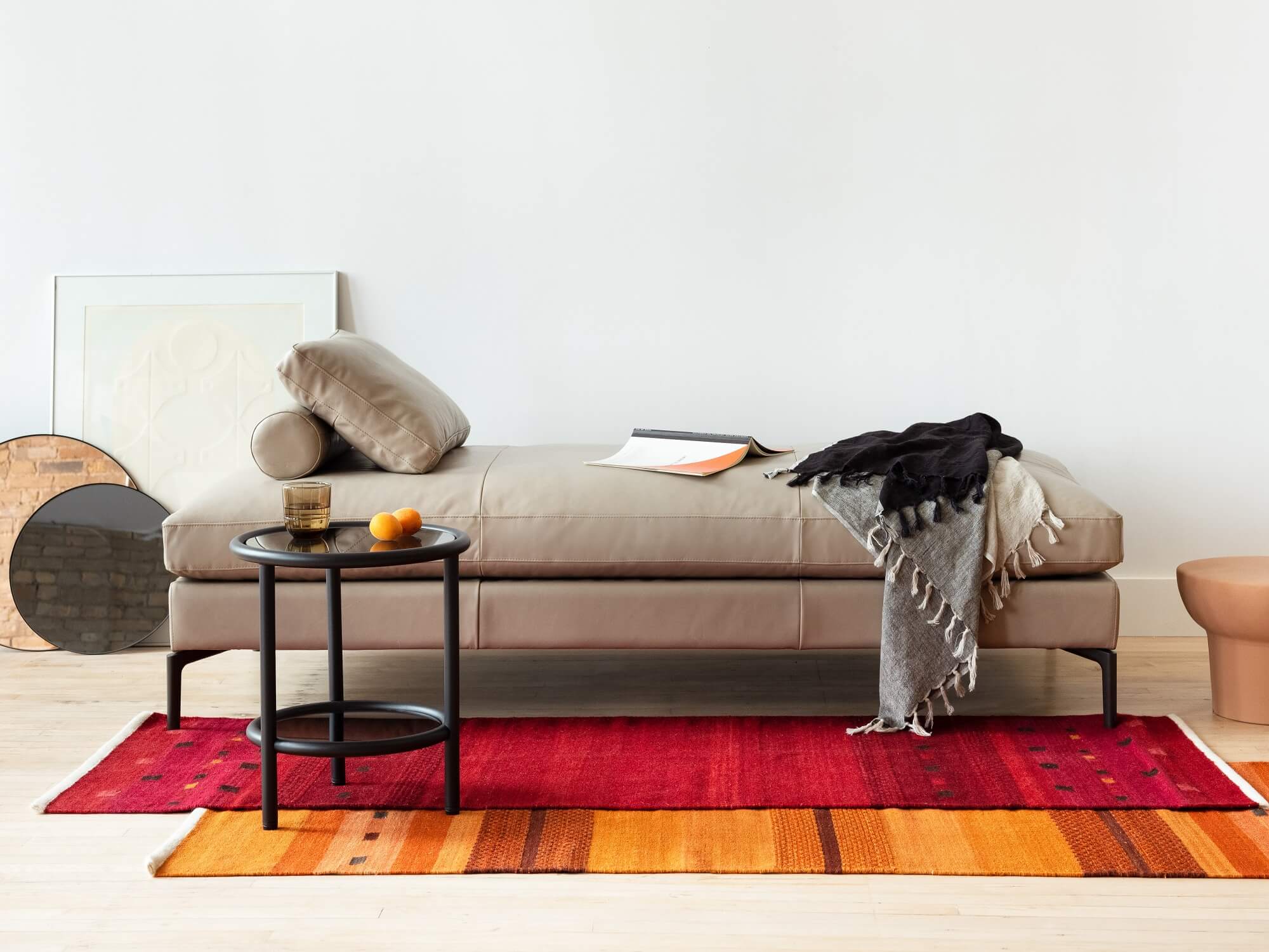 Black round end table with gray leather chaise and red and orange runner rugs