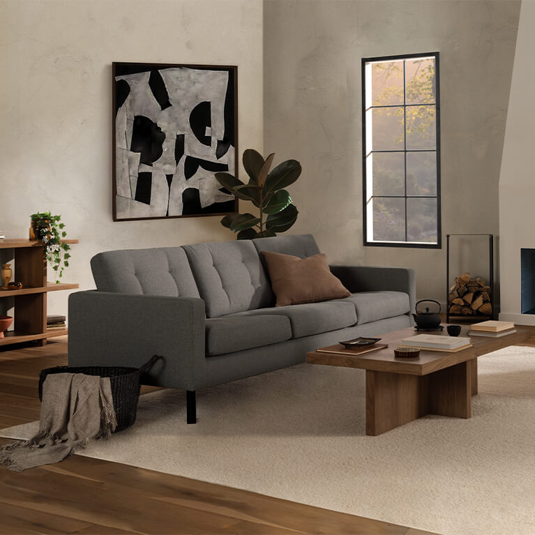 Grey fabric sofa is displayed in a modern living room with a walnut table. Link to seating category