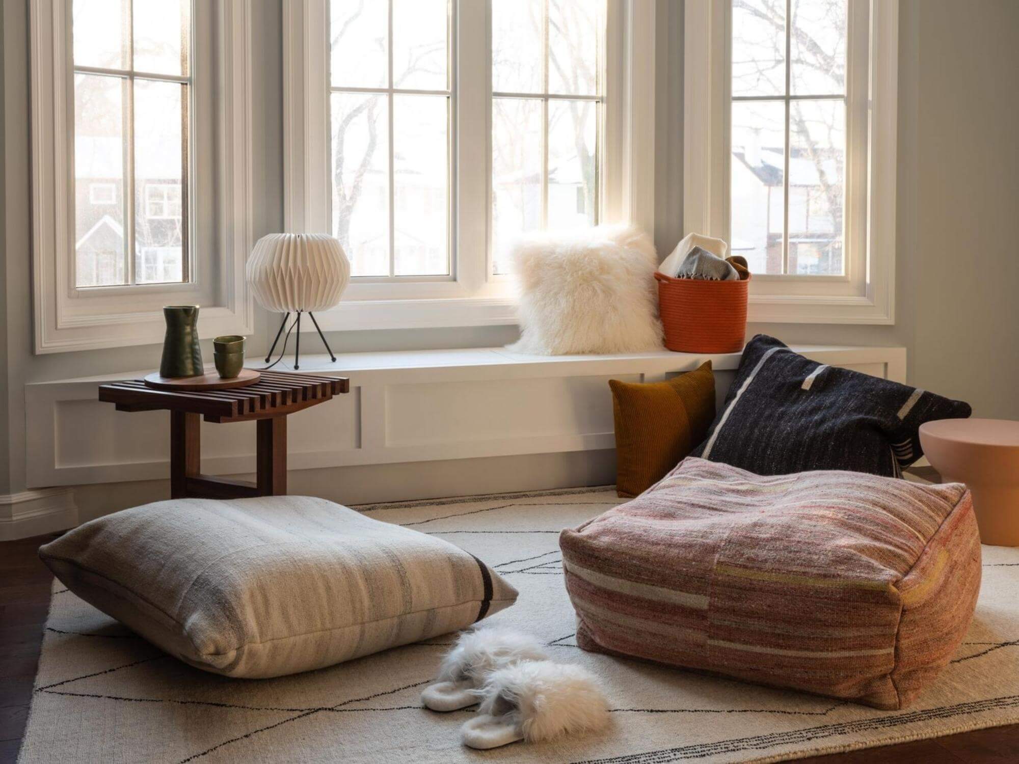 Slatted walnut end table beside floor pillows and sheepskin throw pillow