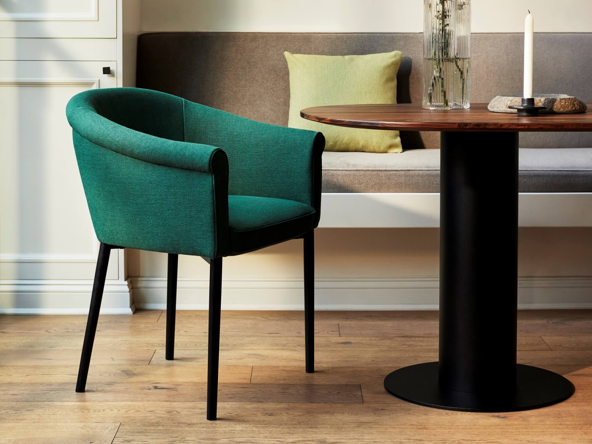 Green upholstered dining chair pulled up to walnut rounded dining table with bench