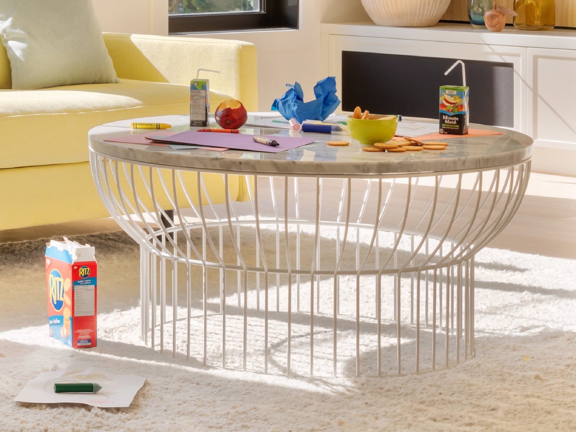 Front view of round white wire coffee table with kids' snacks and crafts on top