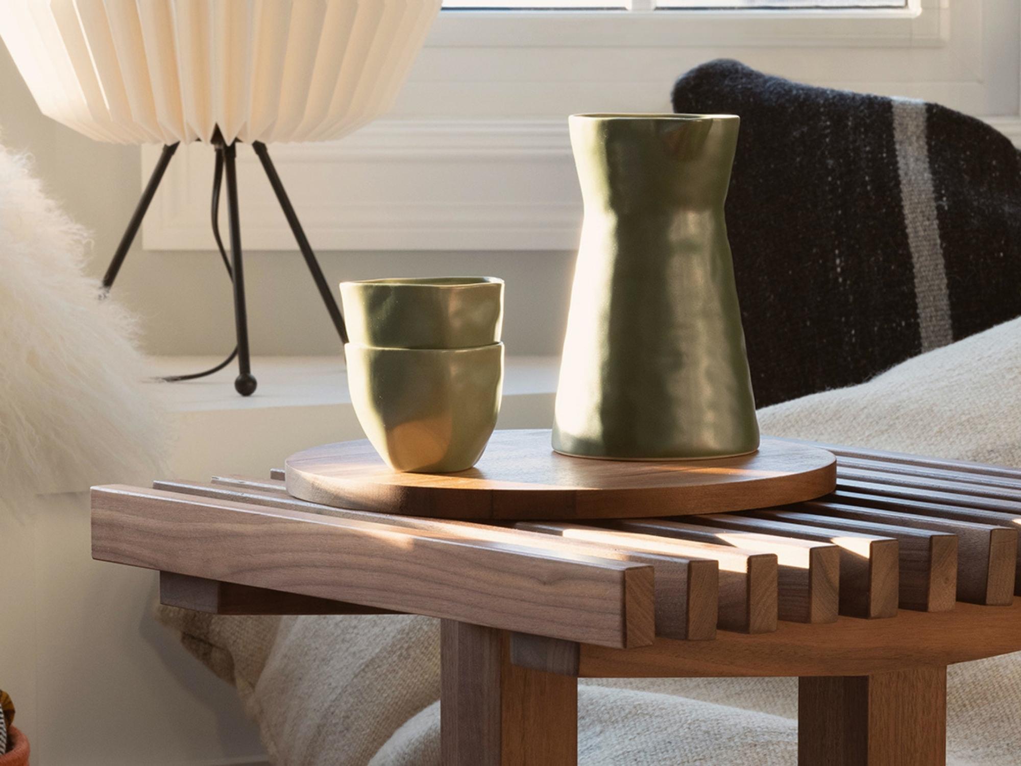 Green stoneware tumblers and vase on slatted walnut side table with floor pillows