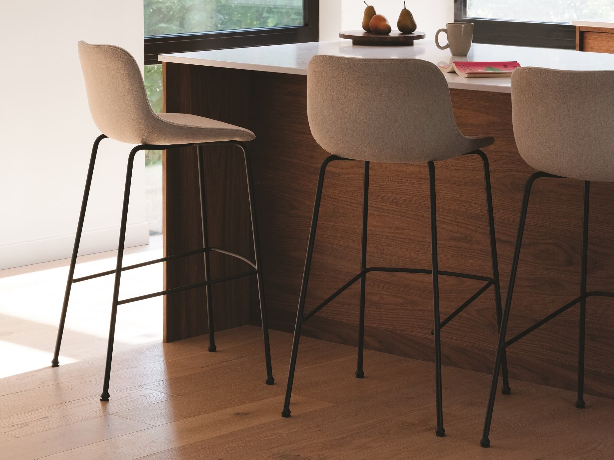 Three beige upholstered counter height stools at modern walnut counter