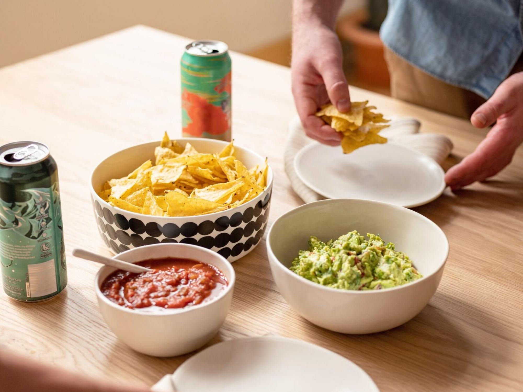 White stoneware bowls and plates with chips, guacamole, and salsa