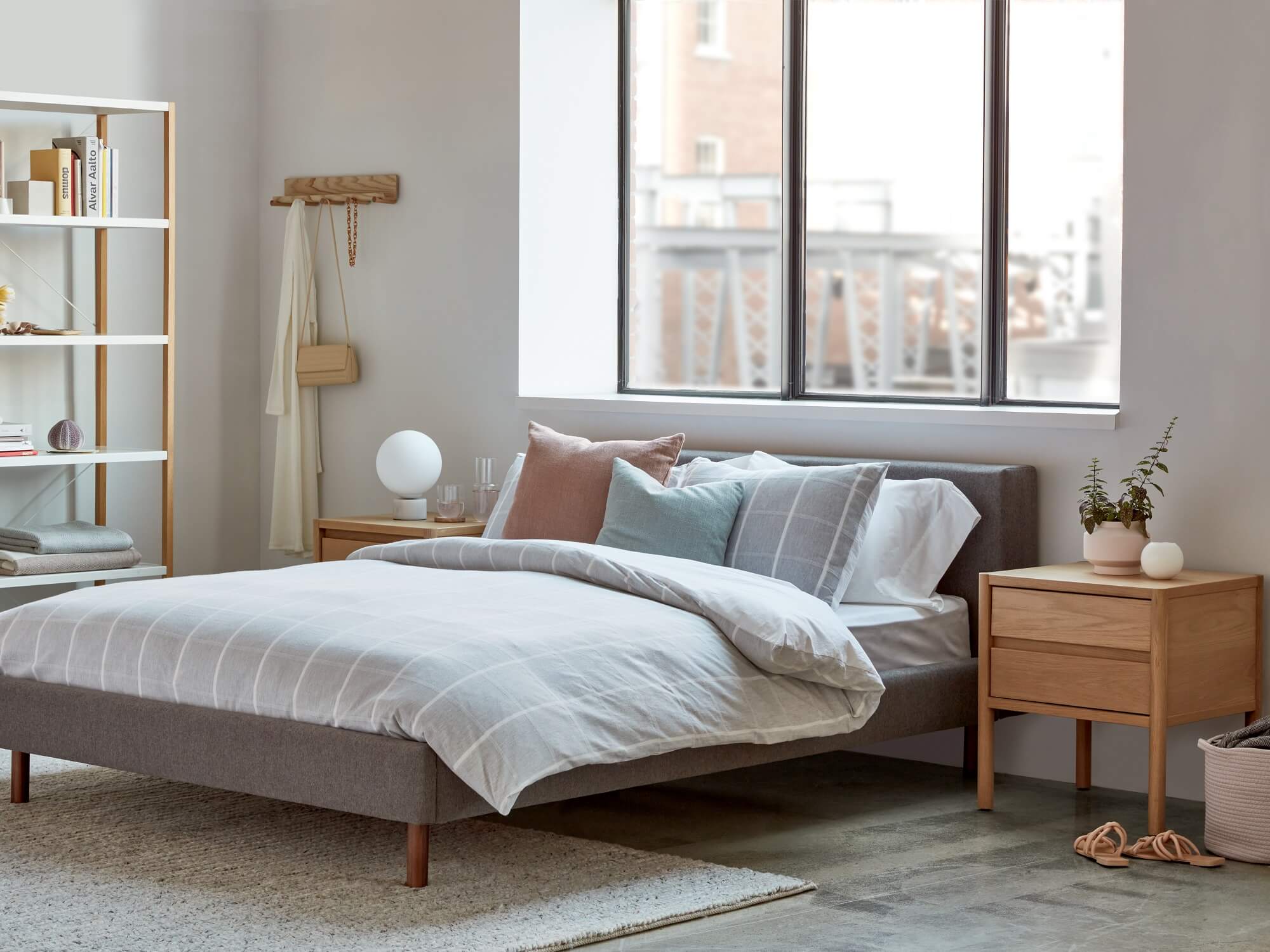 Oak nightstand beside grey upholstered bed in bright bedroom