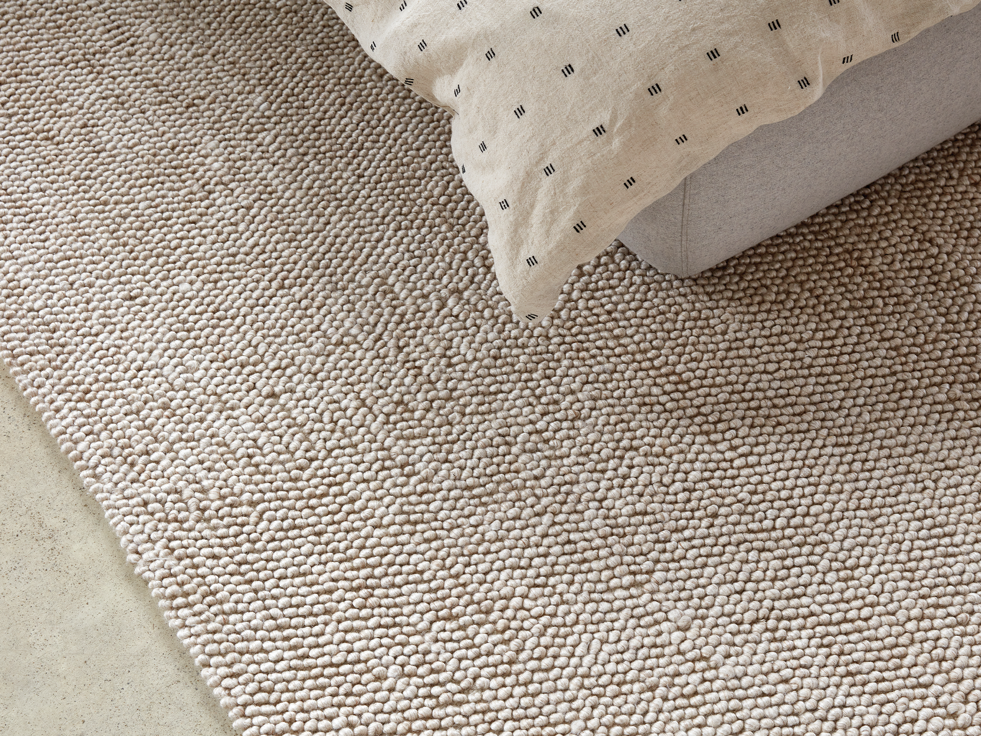 Beige braided wool rug under a grey upholstered bed and beige duvet set