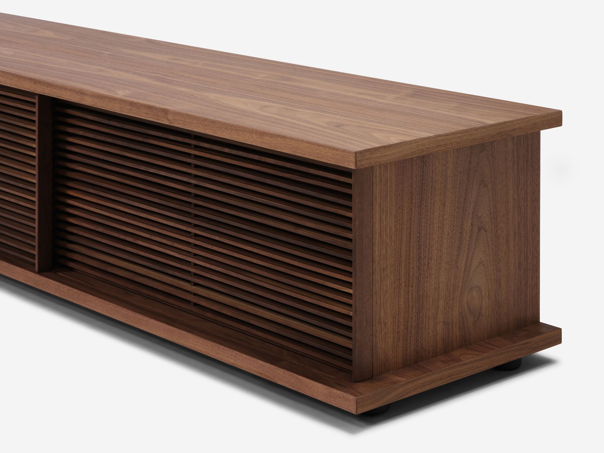 Angled view of the Plank mid century media console in walnut with slats