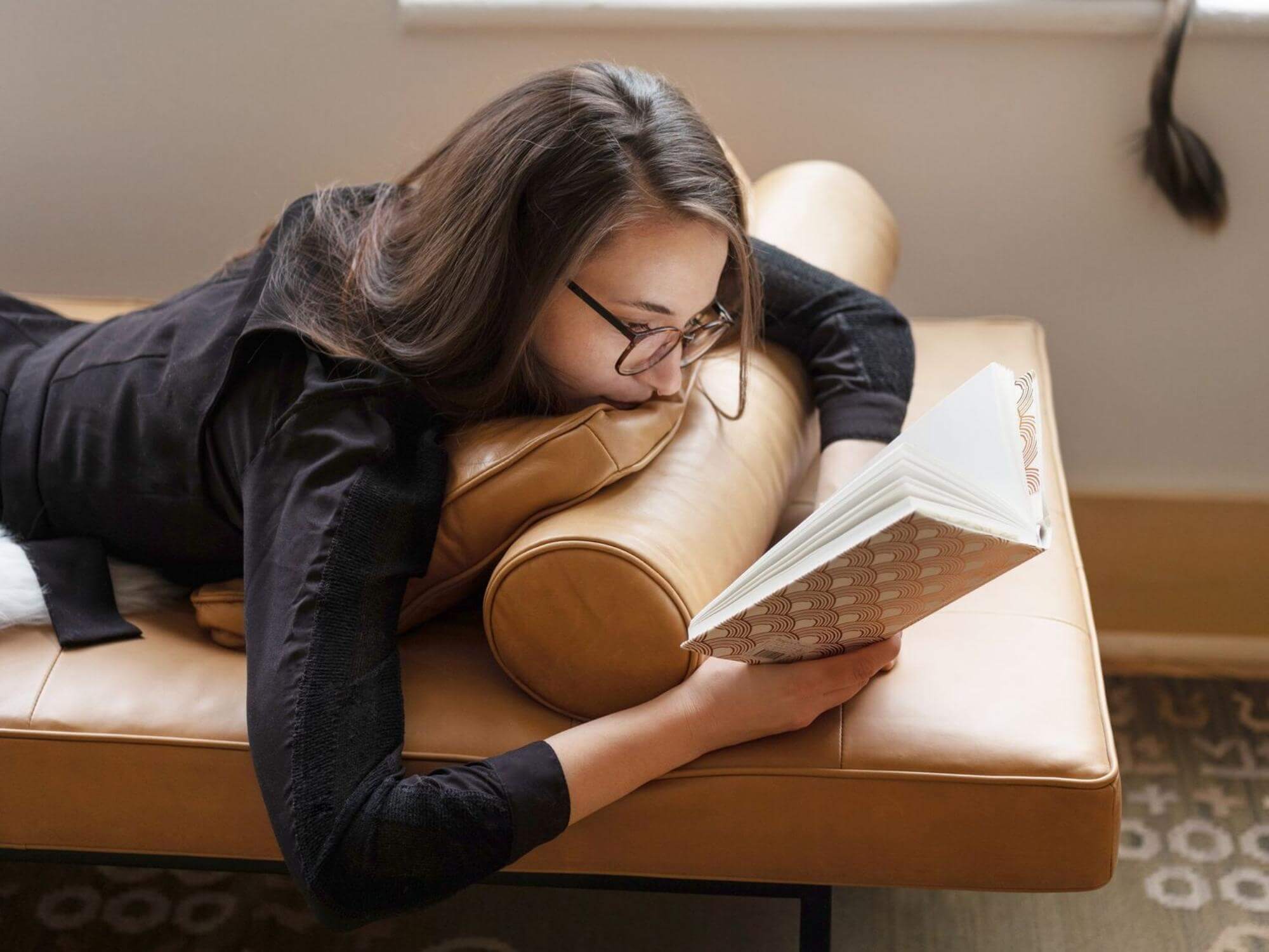 Woman reads on leather daybed with matching bolster pillow