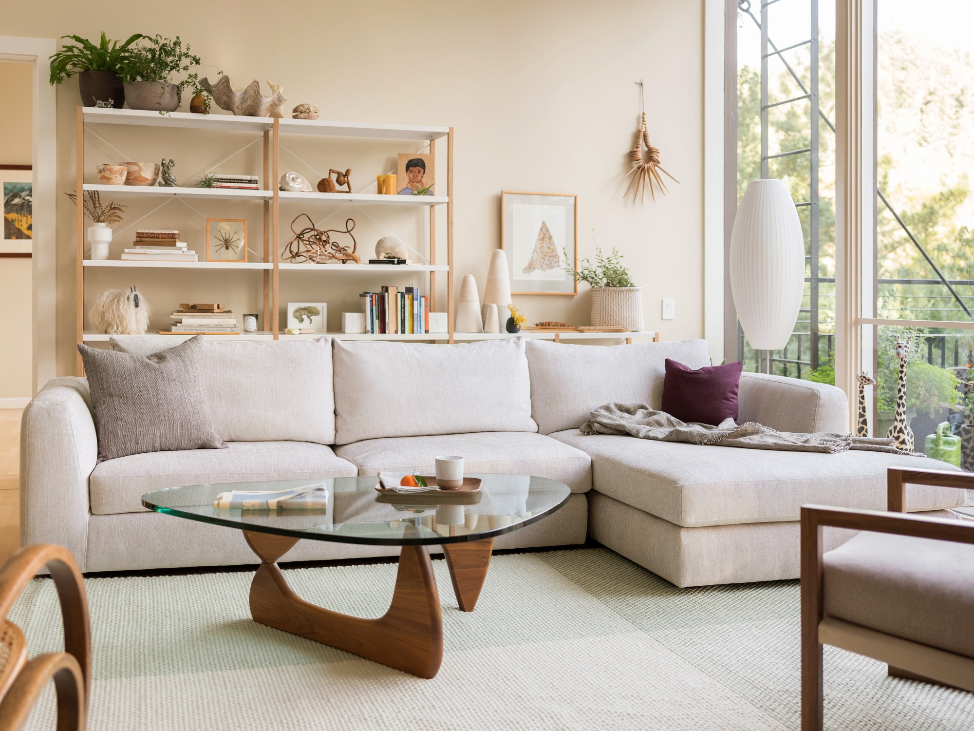 Beige sectional in living space with bookshelf and mid mod coffee table