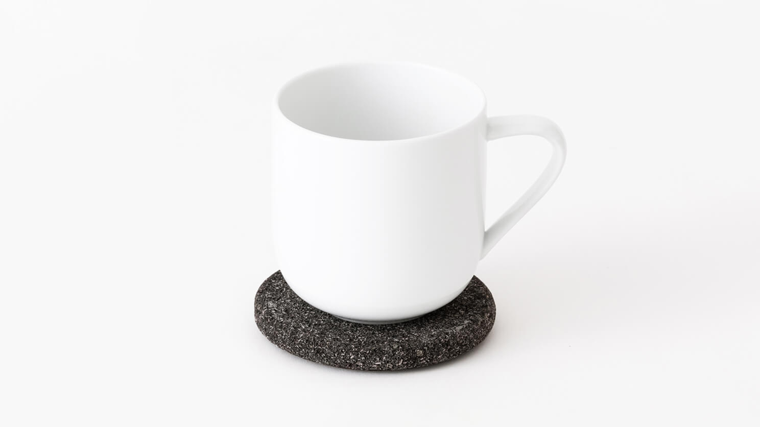 A white mug sits on one modern coaster in lava stone