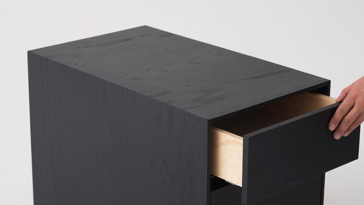 Top detail view of black oak filing cabinet with hand opening drawer