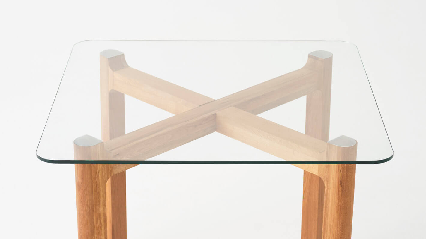 Detail view of the Place square contemporary dinette table with clear glass top and oak legs