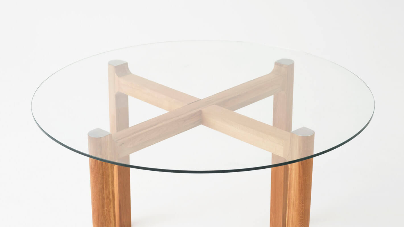 Detail view of the Place round contemporary dinette table with clear glass top and oak legs