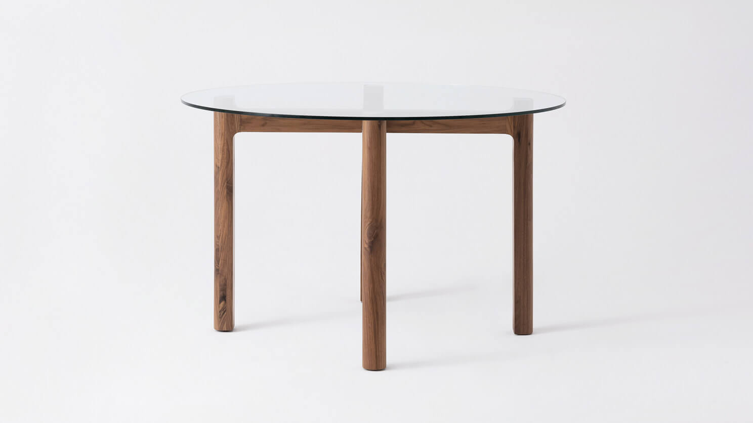 Side view of the Place round contemporary dinette table with clear glass top and walnut legs