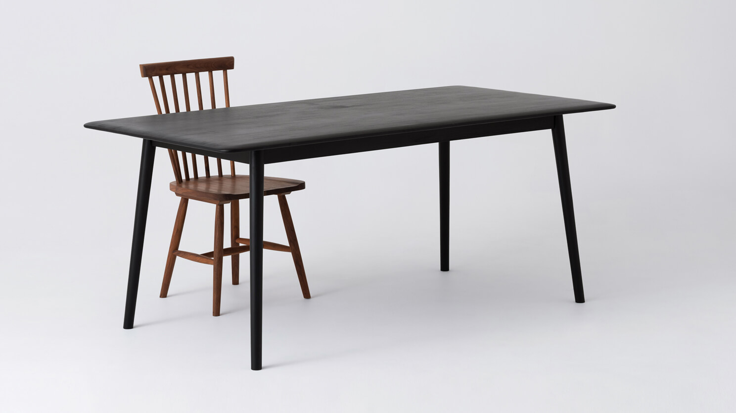 Angled view of the medium sized Kacia solid wood dining table in black with red chair