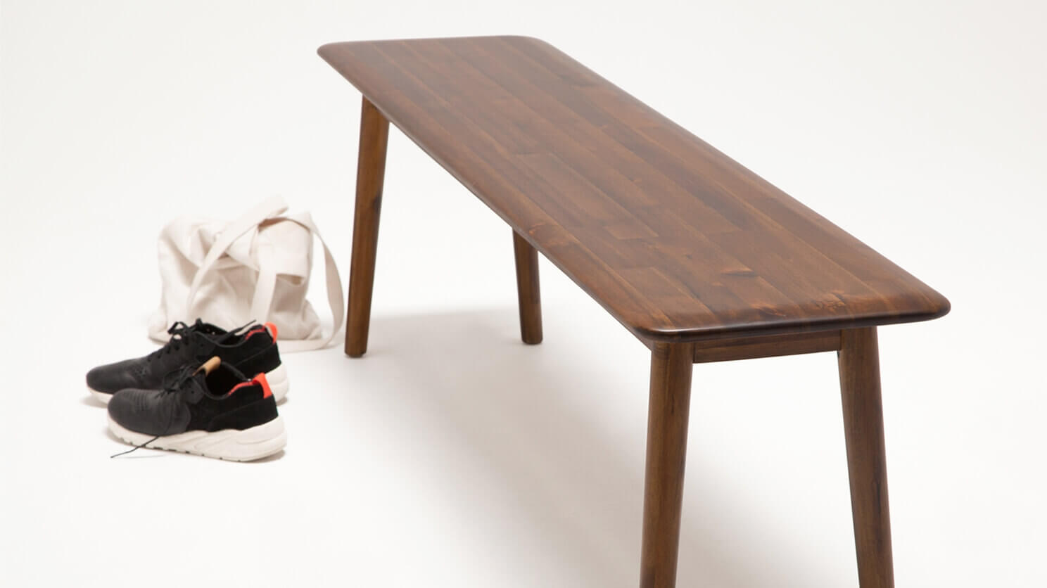 The Kacia wooden dining bench in java beside sneakers and a tote bag