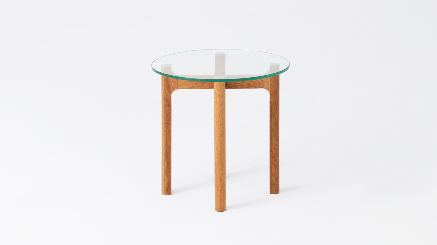 Side view of the Place round accent table with clear glass top and oak legs