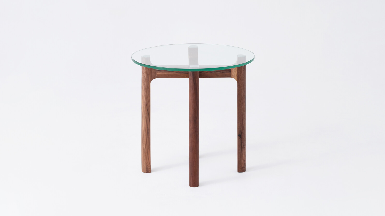 Side view of the Place round accent table with clear glass top and walnut legs