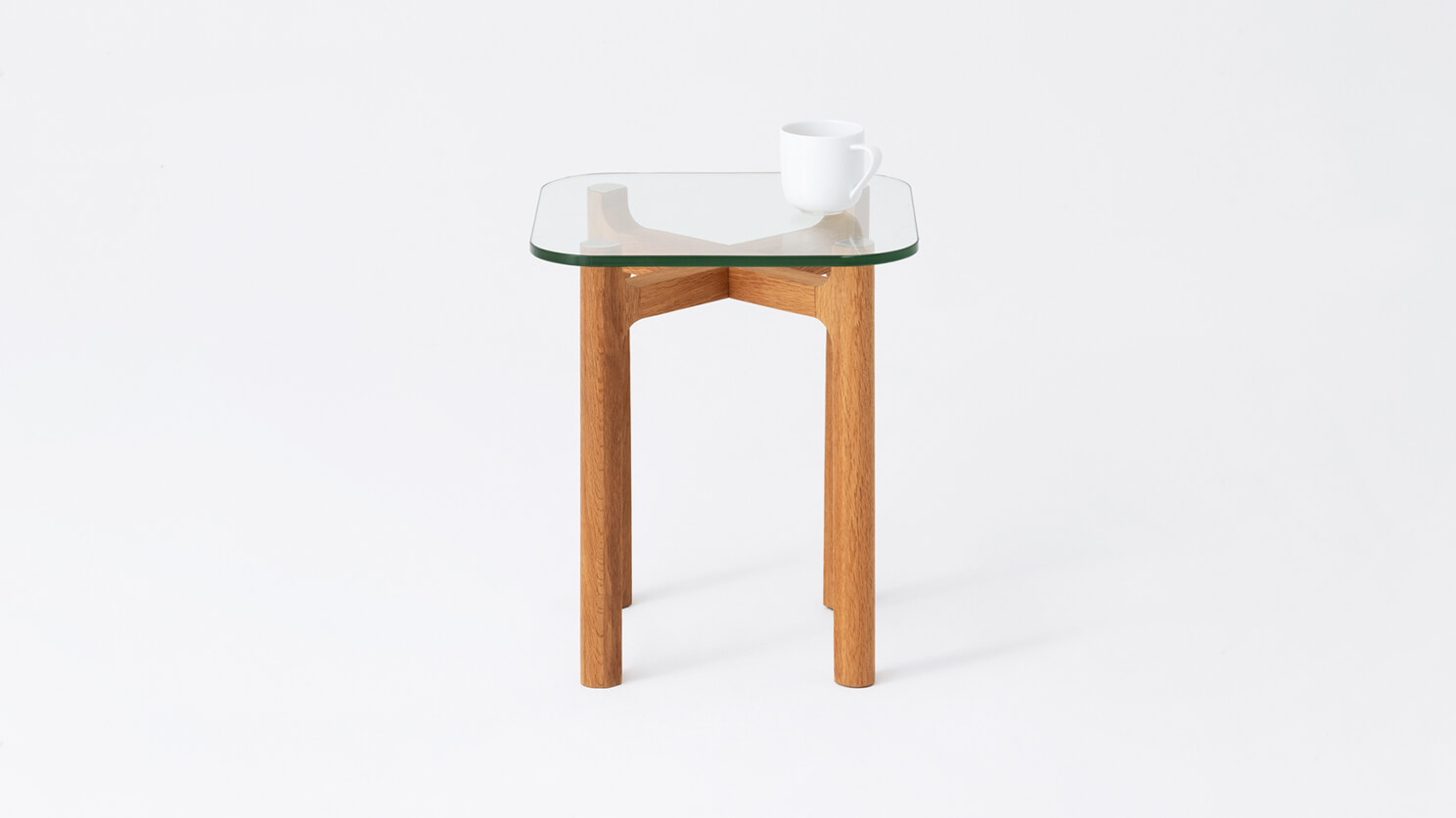 Front view of the Place square accent table with clear glass top and oak legs with a coffee cup on it