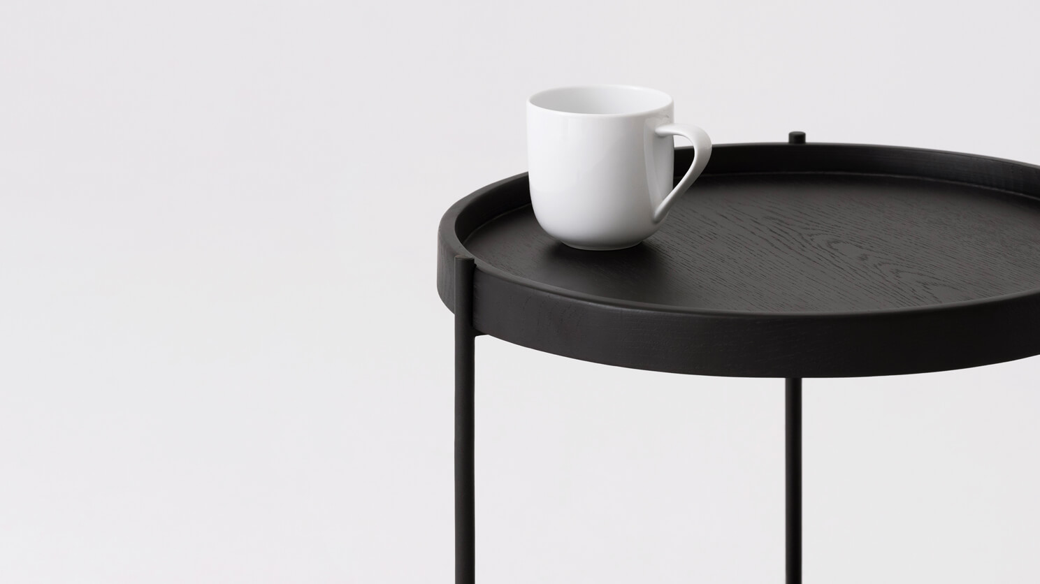 Detail view of the Sage modern round end table in black oak with a coffee cup on it