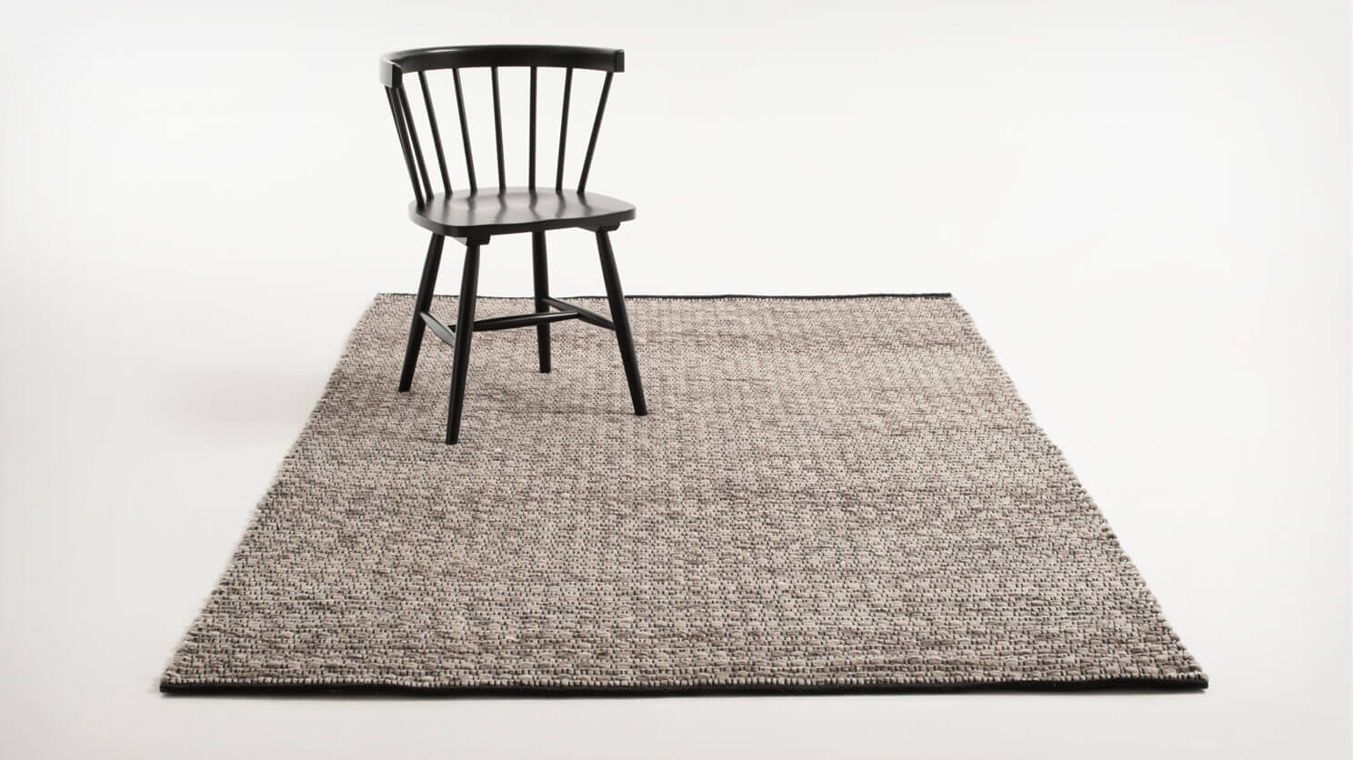 Angled view of the Husky braided rug with a black dining chair on it