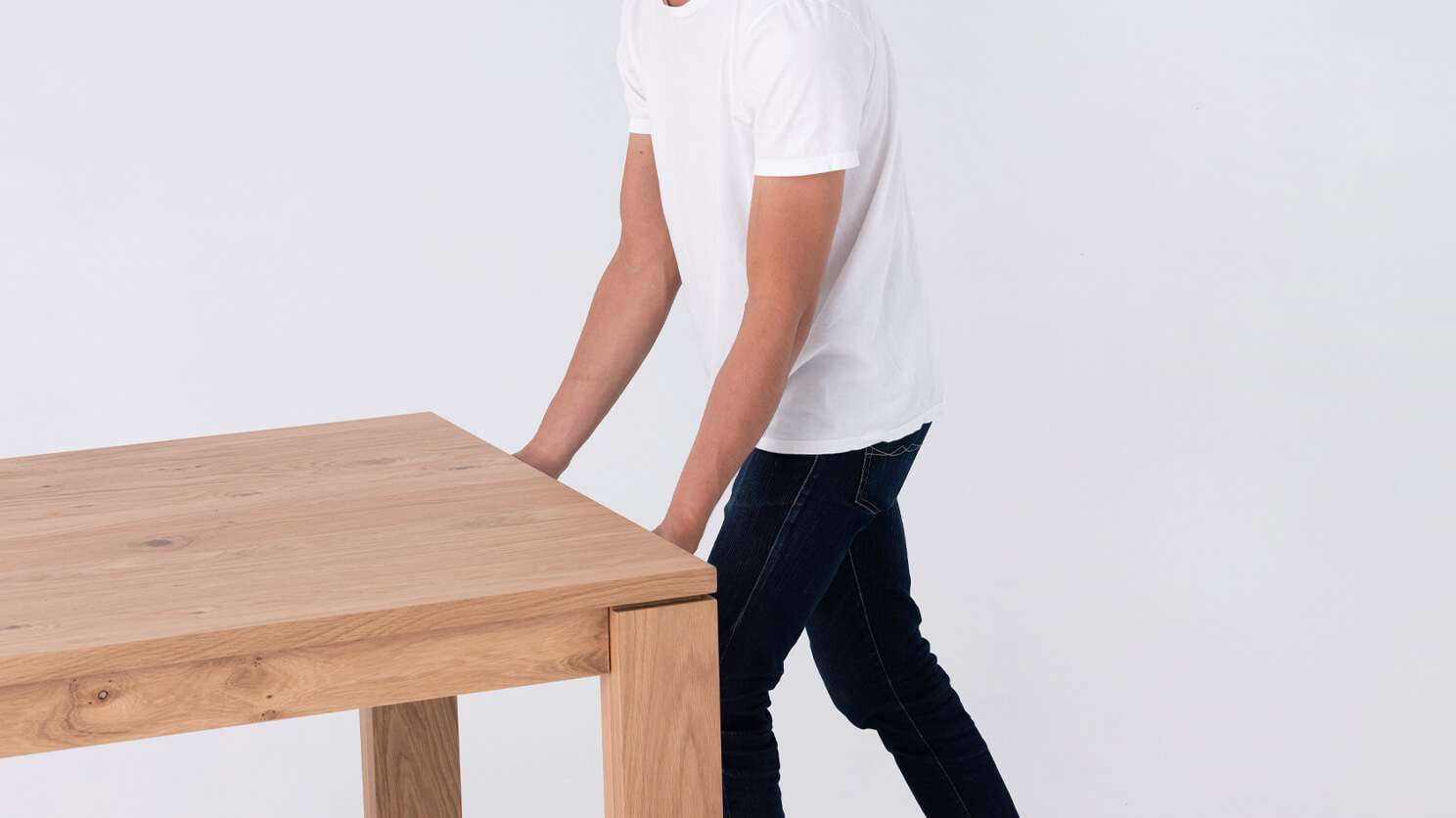 A man grabs the edge of the Bon solid wood dining table in oak