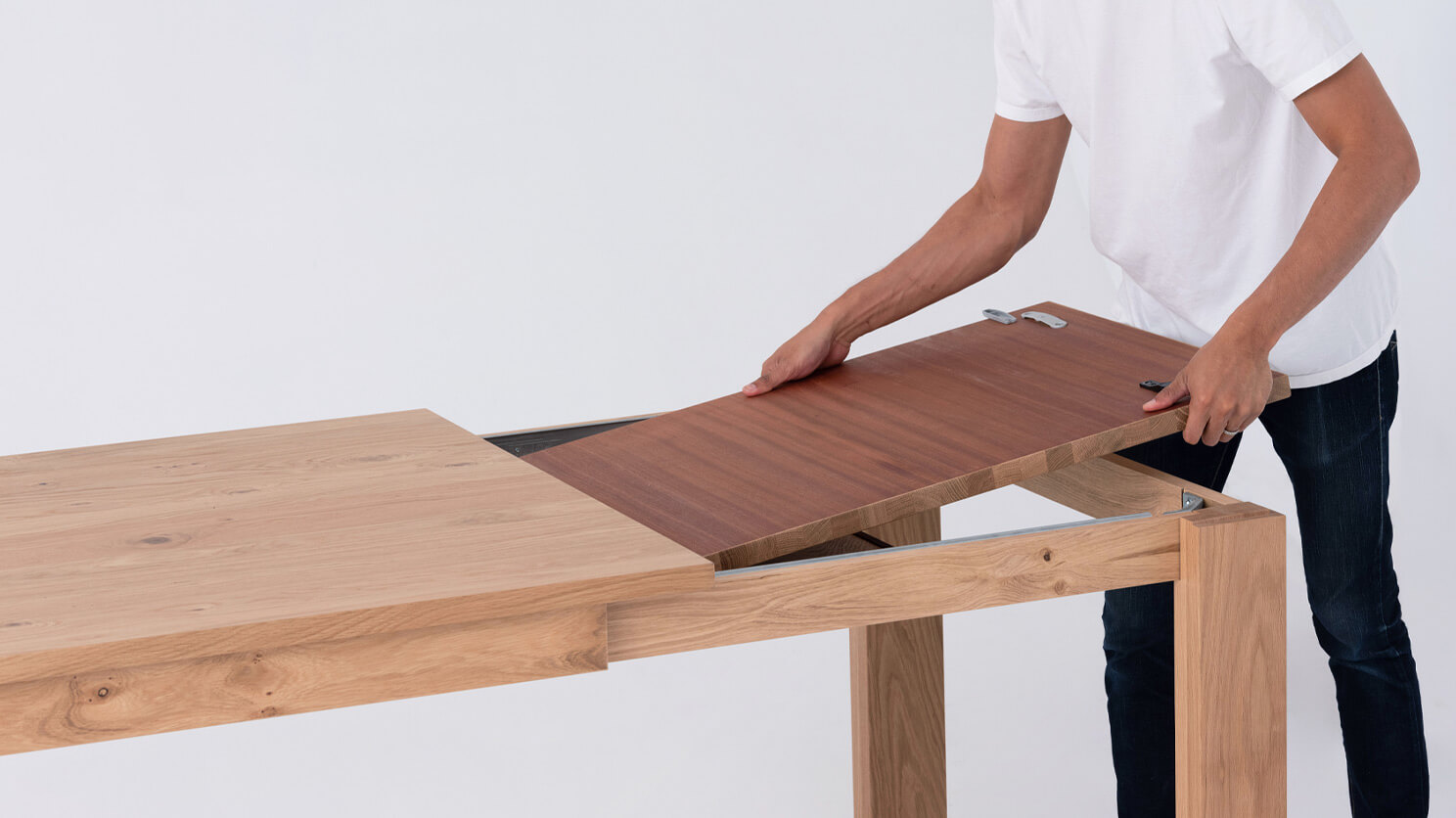 A man pulls out the leaf of the Bon solid wood dining table in oak