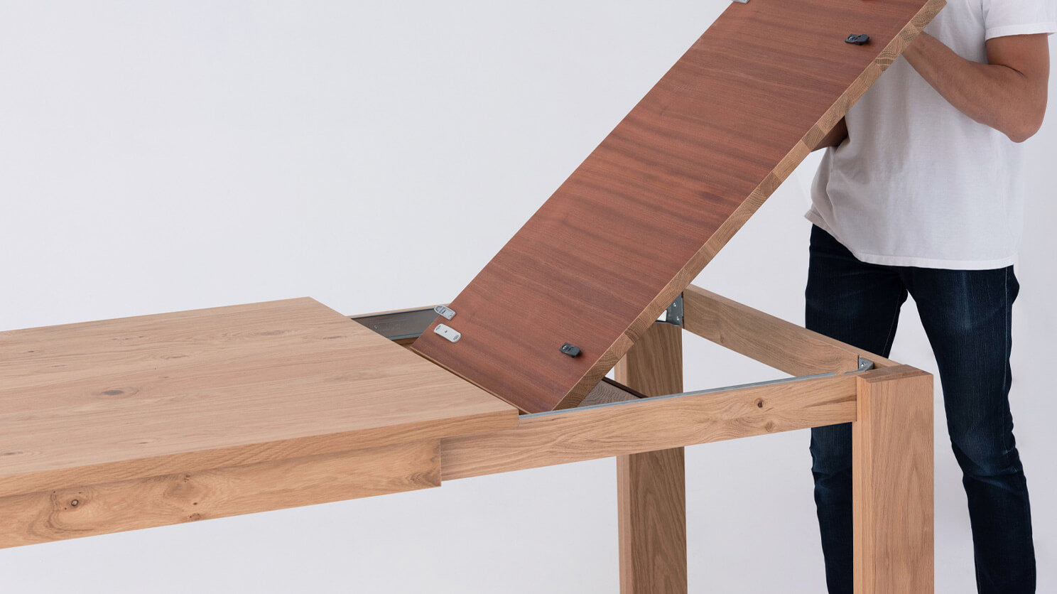 A man lifts out the leaf of the Bon solid wood dining table in oak