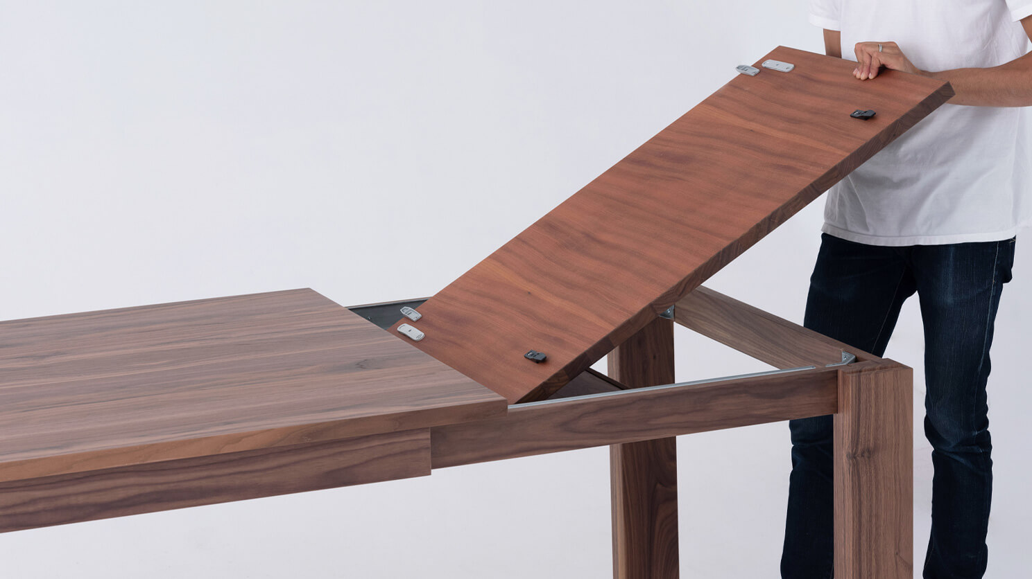 A man lifts out the leaf of the Bon solid wood dining table in walnut