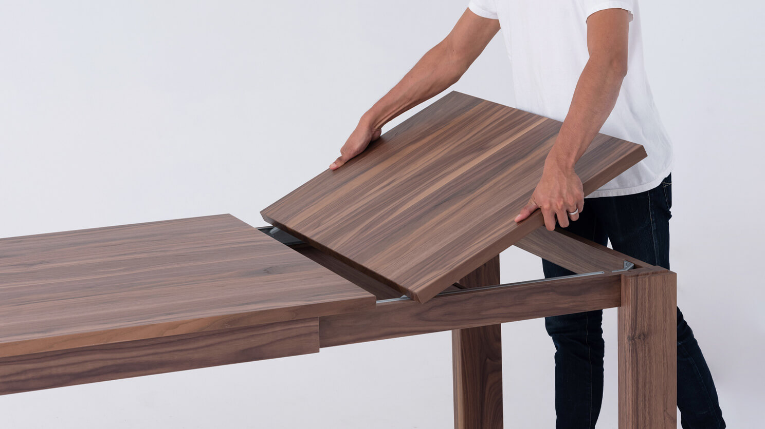 A man places the leaf of the Bon solid wood dining table in walnut