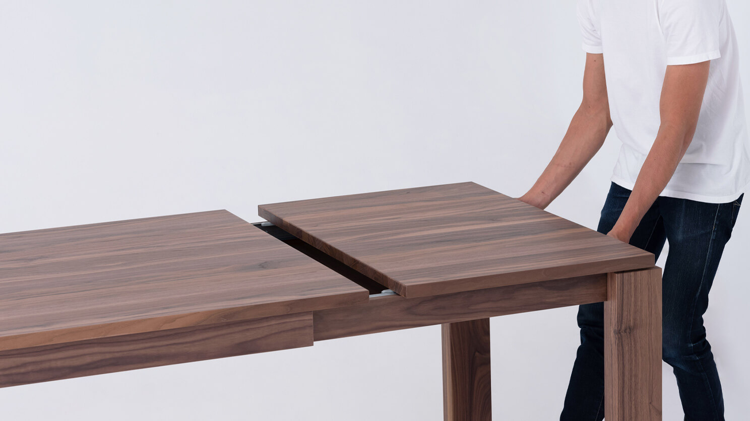 A man pushes the Bon solid wood dining table in walnut together to add the leaf