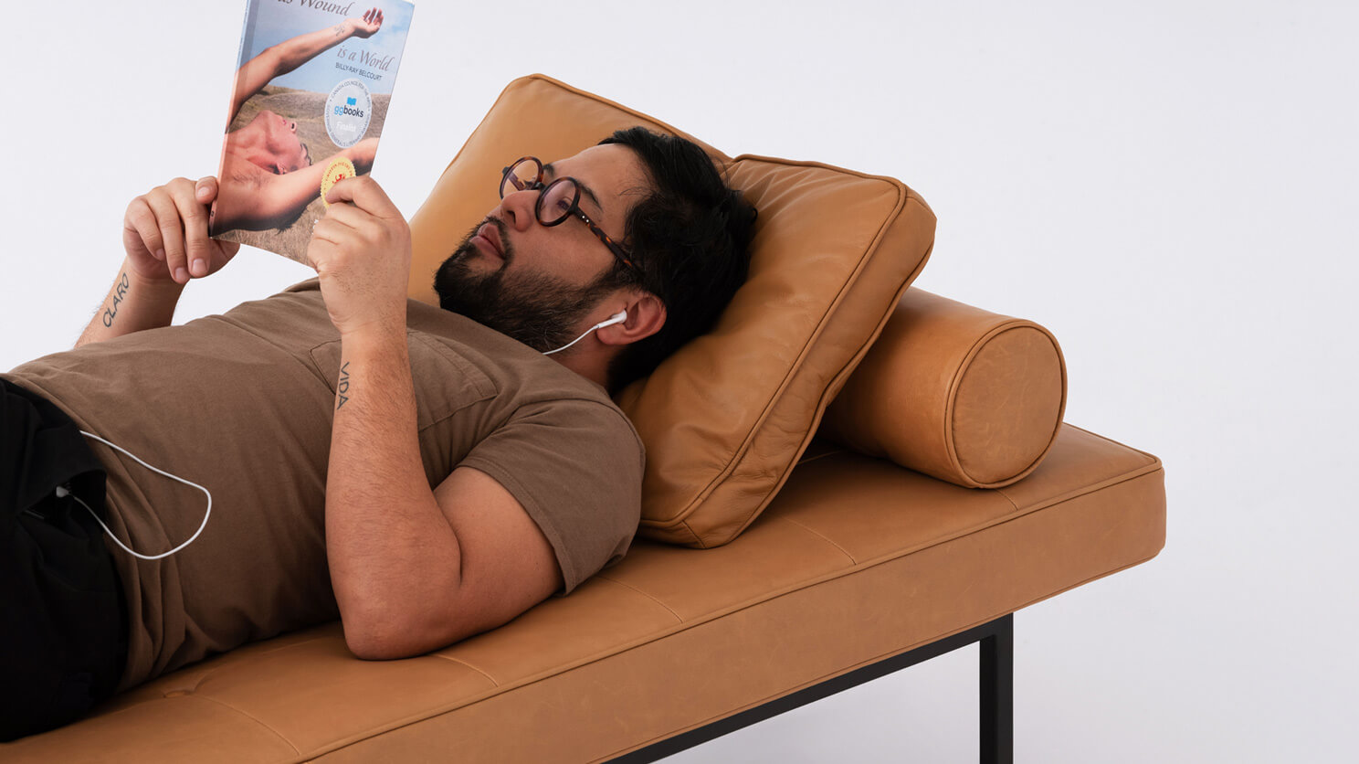 A man reading a magazine relaxes on the Bank daybed in brown leather