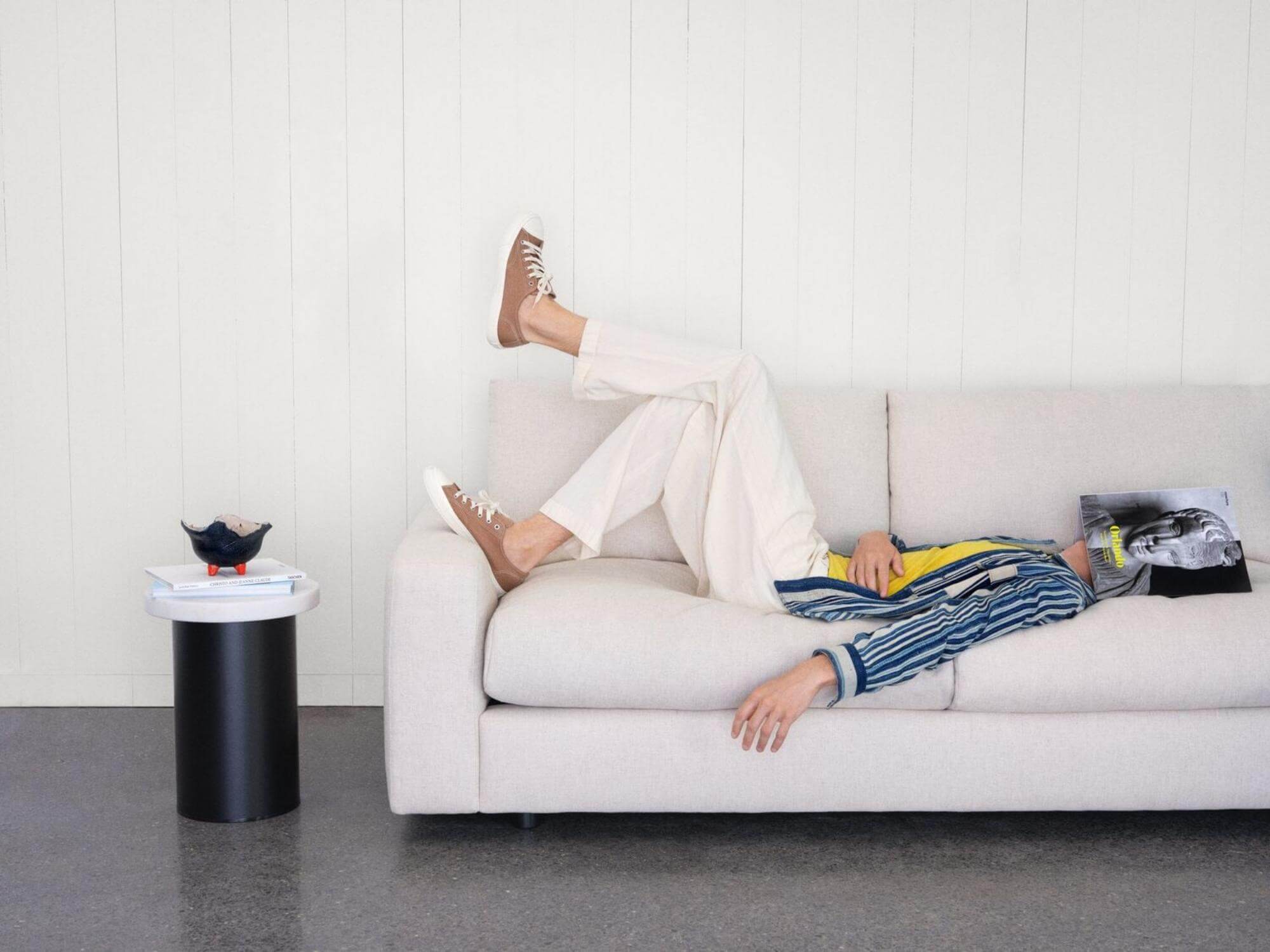 Man reclines on cream sofa with magazine over his face