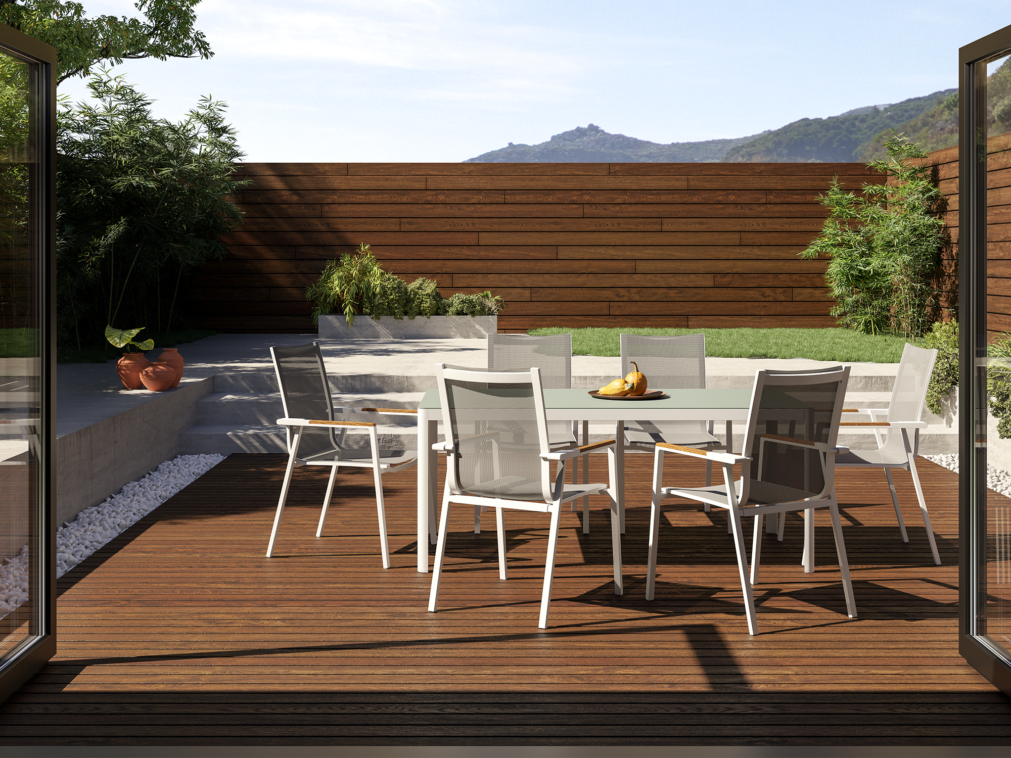 A white and teak outdoor dining table and dining chairs sit on a dark wood deck